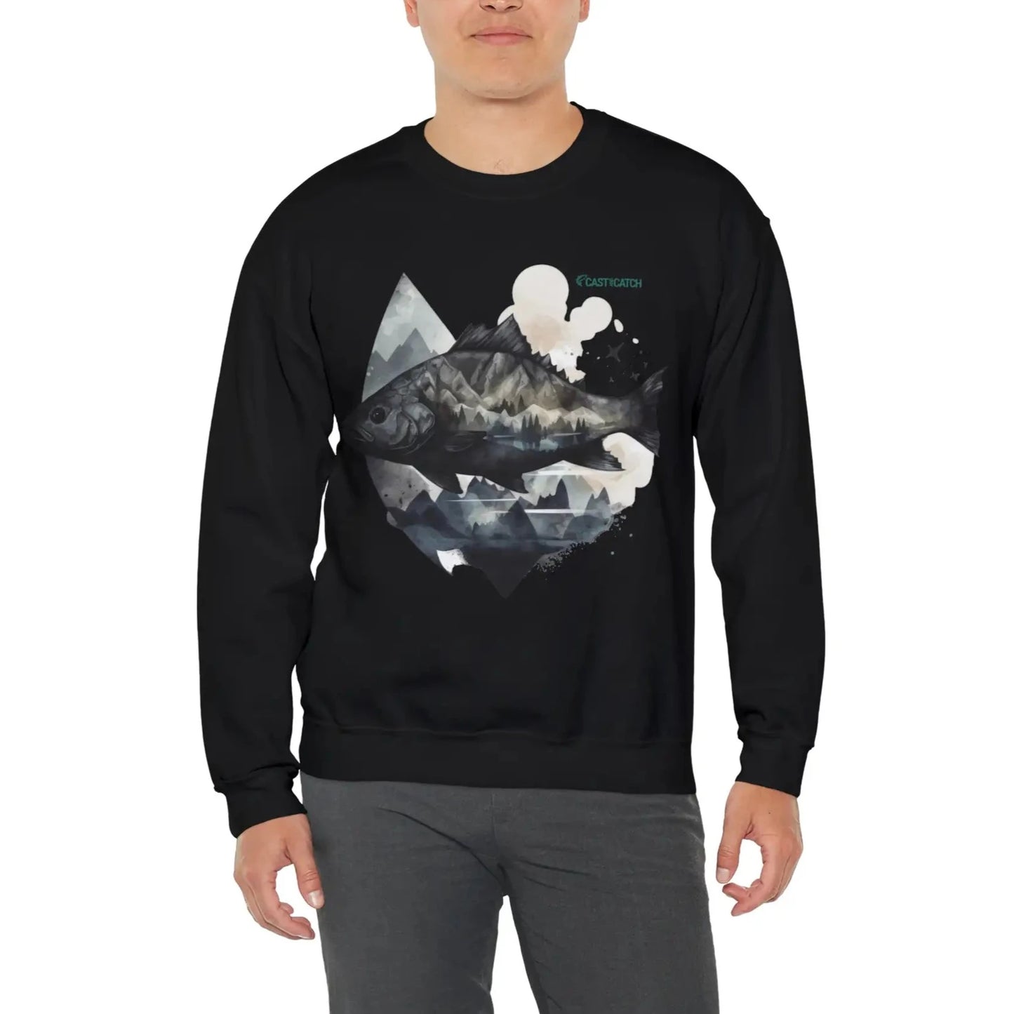 Fishing sweatshirt color black, context man wearing sweatshirt. Print design on the front side, of a big fish, with reflection and background of misty grey mountains. Brand logo in Plankton Green above the design, on the left side.