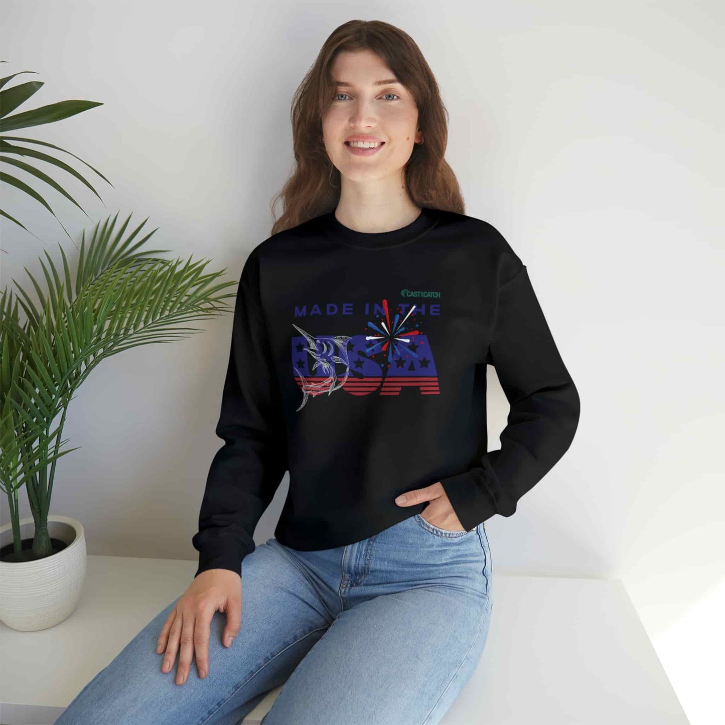 Fishing sweatshirt color black, context female model. Front is designed with the text 'made in the USA' in US flag colors, with a Marlin fish white print on it. Brand logo in Plankton Green above the design, on the left side.